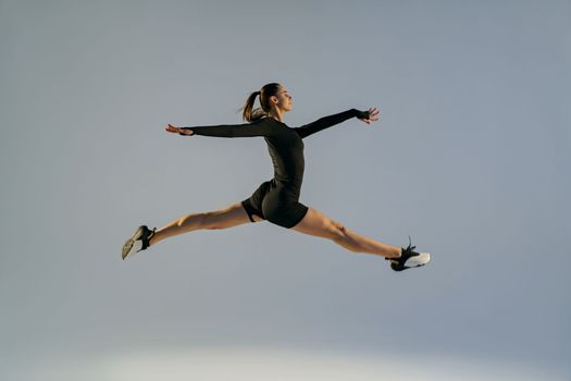 Sporty girl jumping doing split leap in air with joyful expression. Flexible and weightless concept