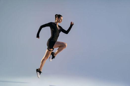 Smiling sporty woman running in Mid-Air exercising during cardio workout over studio background