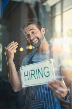 Were looking for the best baristas in town. Portrait of a handsome young man hanging up a hiring sign on the door of his store.