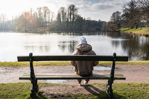 Contemplation by the Lake. A Young Woman Sitting on a Park Bench