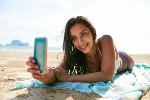 Beach selfies. a young woman taking a selfie while lying on the beach.