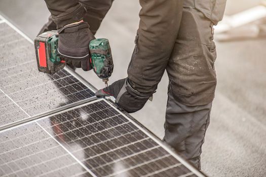 The solar panel installer twists the modules together using aluminum fasteners and a cordless drill. Rooftop installation work and security, concept with copy space