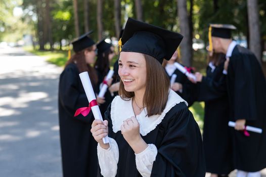 Group of happy students in graduation gowns outdoors. A young girl is happy to receive her diploma.
