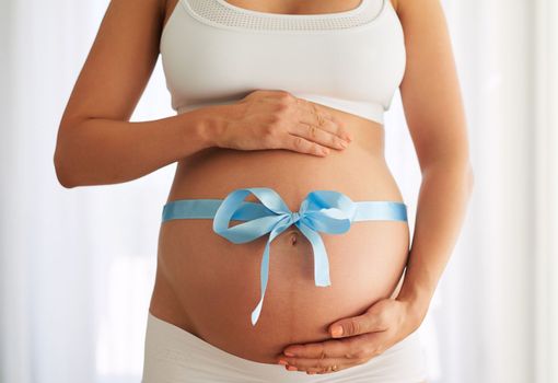 Theres no bigger gift. a woman with a blue ribbon tied around her pregnant belly.