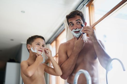 This is the tricky part. a handsome young man teaching his son how to shave in the bathroom.