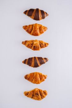 Flat lay of several delicious brown and chocolate croissants laid out in a line on a white table
