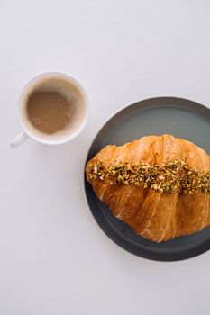 Flat lay of cup of cappuccino with pistachio croissant on the white table