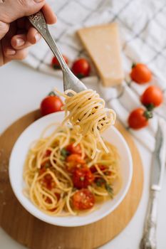 Spaghetti wrapped on a fork in the background of a portion of pasta with cherry tomatoes in a plate and parmesan cheese