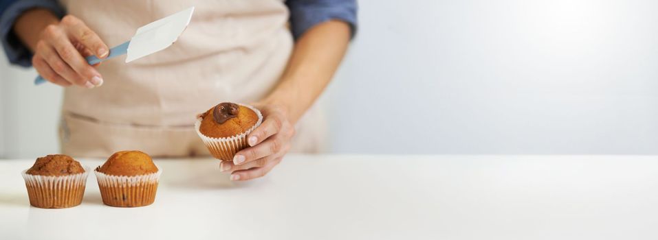 Chef, cupcakes and person icing muffin with mockup or copy space isolated against a white background. Closeup, hands and cook preparing and decorating dessert or treat on a kitchen table