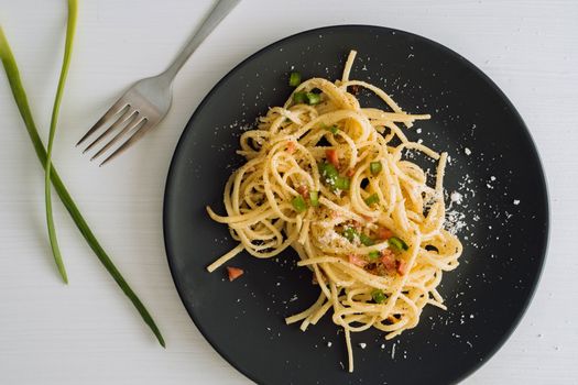Spaghetti pasta sprinkled with cheese parmesan and green onions on a black plate on a white table with fork