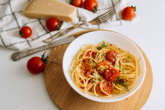 Close up portion of spaghetti pasta with parmesan and cherry tomatoes sprinkled with spices in a plate on a wooden board