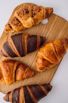 Flat lay of bunch of appetizing brown and chocolate croissants on a wooden board on white table