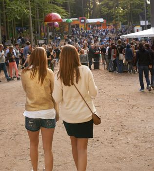 The party starts here. Rear view shot of two friends walking together at an outdoor festival.