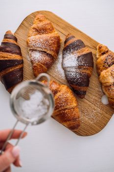 Flat lay of appetizing brown and chocolate croissants are sprinkled with powdered sugar