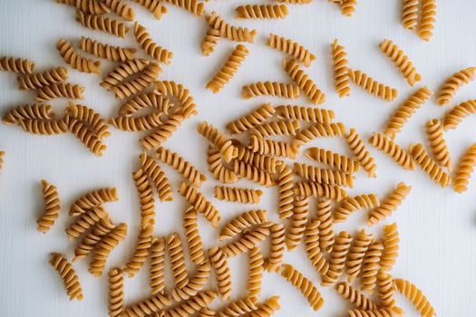 Flat lay of scattered many wavy pasta from whole wheat flour on white table