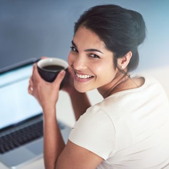 All I need is a little coffee. High angle portrait of an attractive young businesswoman drinking coffee while working on a laptop in her office.