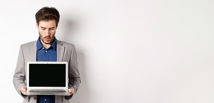 Handsome caucasian businessman in suit showing empty laptop screen, demonstrate promo, standing on white background
