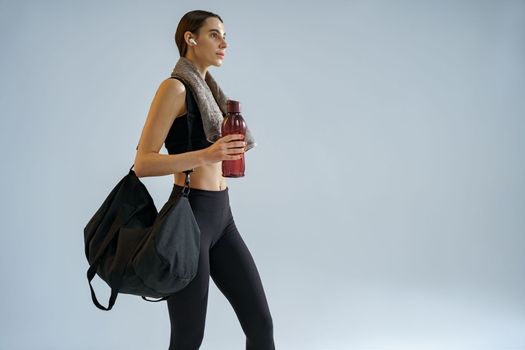 Tired sporty woman with sports bag and bottle of water after training on studio background