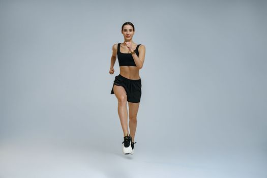 Sporty determined woman wearing sportswear running during cardio workout over studio background