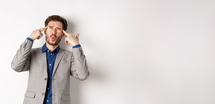 Distressed and tensed businessman pointing at head and complaining, feeling annoyed with situation blowing his mind, standing bothered on white background