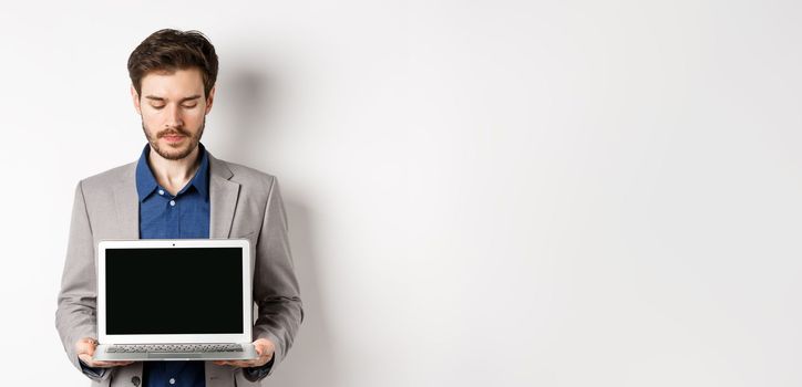 Handsome caucasian businessman in suit showing empty laptop screen, demonstrate promo, standing on white background