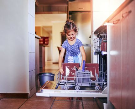 Shes a good little housekeeper. an adorable little girl loading the dishwasher on her own at home.