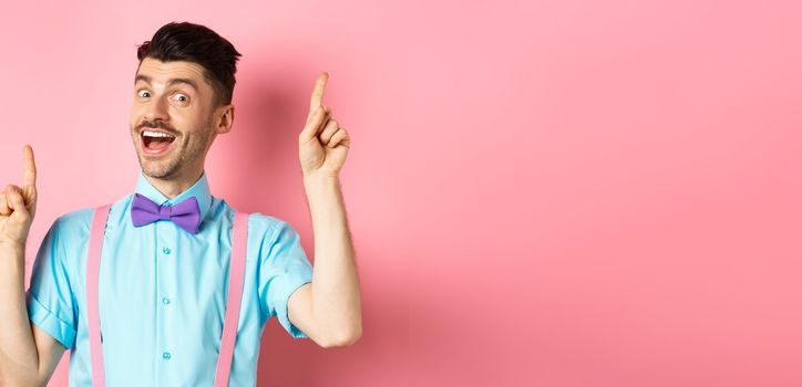 Cheerful guy with french moustache pitching an idea, dancing and raising fingers up, having solution, standing happy over pink background