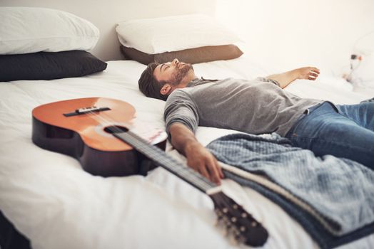 Quick nap before I start playing again. a young handsome man sleeping next to his guitar at home.