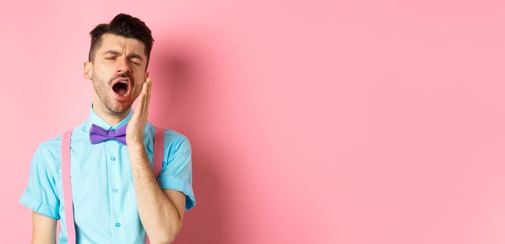 Image of tired guy in bow-tie yawning with opened mouth and closed eyes, standing sleepy, feeling fatigue, standing over pink background