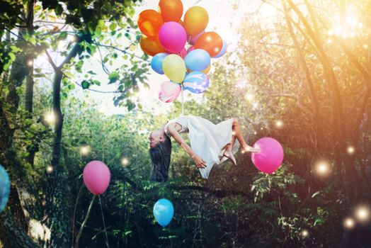 Set your imagination free. a little girl floating in the air with helium balloons around her waist in a forest.