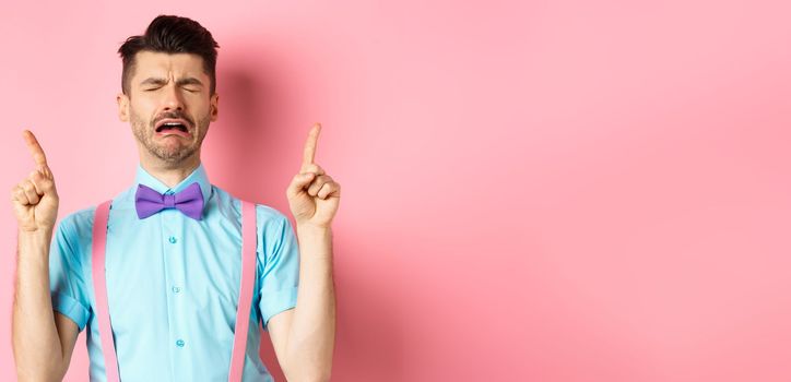 Sad and miserable guy sobbing and crying, pointing fingers up and something disappointed, standing upset on pink background