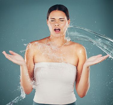 Cleaning, grooming and woman surprised with a water splash isolated on a blue background in a studio. Spa, shower and shocked girl with water for skincare, hydration and dermatology on a backdrop