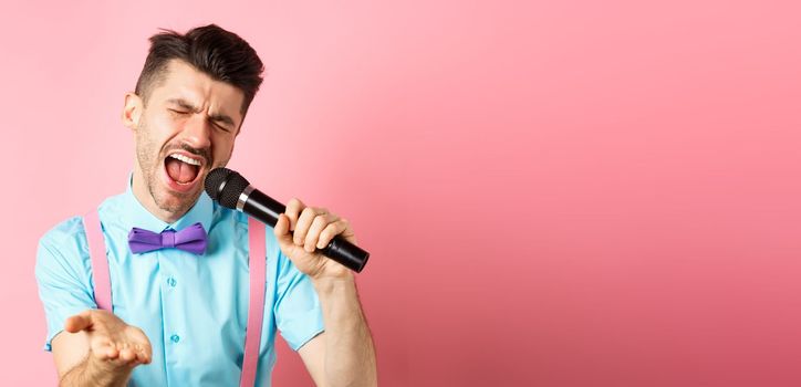 Party and festive events concept. Passionate singer holding microphone and pointing hand at you, singing about love, standing on pink background