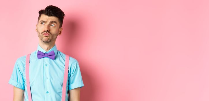 Pensive young man in romantic outfit, looking away and thinking, standing thoughtful on pink background in fancy bow-tie and shirt