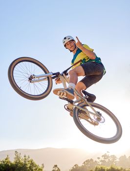 Bike, jump and rock on hand sign with a man bmx rider jumping over a ramp on a trail or course in nature. Sky, mountain and cycling with a male athlete jumping in mid air during fitness exercise