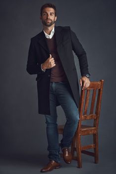 Fashion goals. Studio portrait of a stylishly dressed young man standing next to a chair against a gray background
