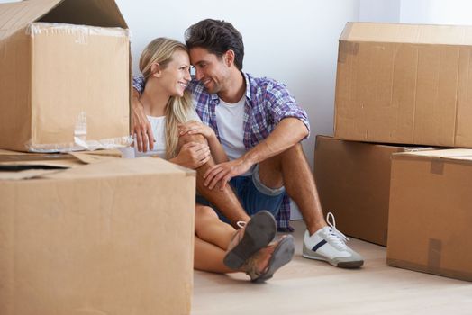 Creating a life together. A happy young couple cuddling while sitting on the floor in their new home and surrounded by boxes.