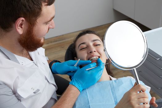 Young Woman checking her beautiful smile in mirror after stomatological treatment