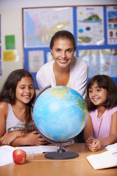 Giving them the world through education. A teacher and two multi-ethnic schoolgirls sitting alongside a globe and smiling at the camera.