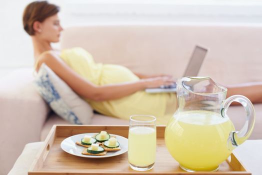 Creating a calm environment around her. A healthy meal next to a pregnant woman lying on the couch with a laptop.
