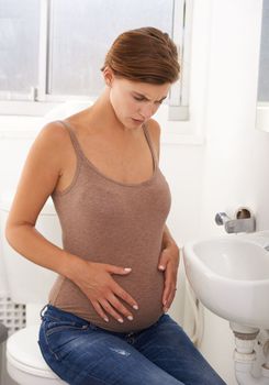 Is this normal. a pregnant woman holding her stomach in discomfort in the bathroom.