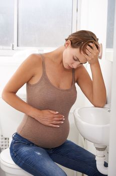 Pregnancy pains. a pregnant woman holding her stomach in discomfort in the bathroom.