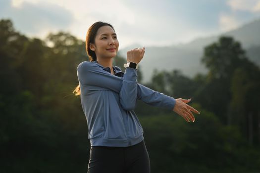 Fitness woman stretching arms before running in the park at evening with sunset. Sport and healthy lifestyle concept.