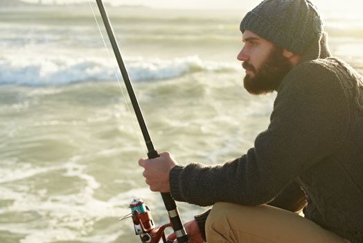 Fishing is his favourite hobby. a bearded man fishing on the beach.