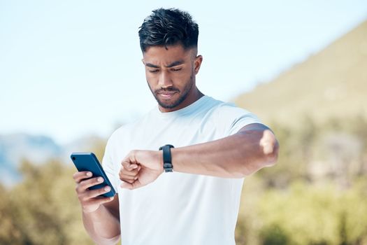 Athletic young man checking his watch after a hike outdoors. Resting while checking time during a workout. Tracking progress during a hike