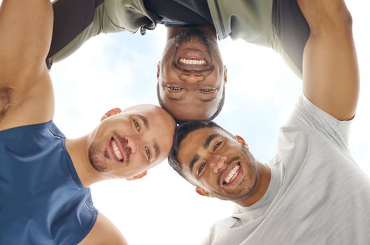Just three buddies building muscles together. Low angle shot of a group of sporty young people joining their heads together in a huddle outdoors.