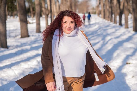 Portrait of an excited red-haired curly fat woman in the park in winter.