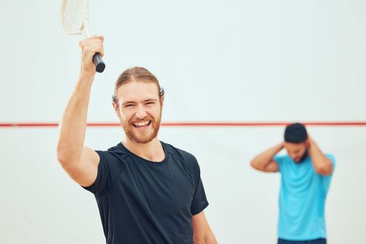 Young athletic squash player winning after playing opponent in competitive court game. Fit active caucasian athlete celebrating success after training challenge in sports centre. Smiling sporty man