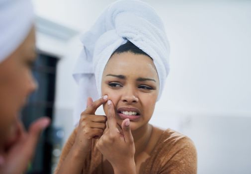 Pimple, begone. a young woman frowning while examining an imperfection on her skin in the mirror.