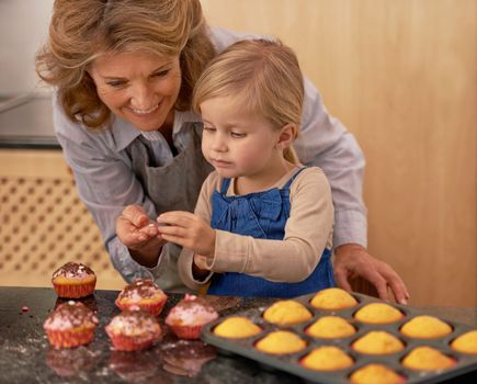 Getting creative with cupcakes. a little girl decorating cupcakes with the help of her grandmother.